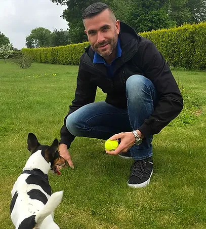 Photo of Jerome outside with a dog and tennis ball.