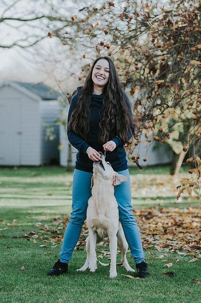 Photo of Anna Bartosik playing with a dog with autumn leaves.