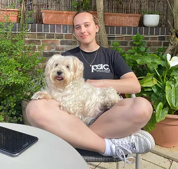 Picture of Toni sitting cross-legged with a dog on their lap